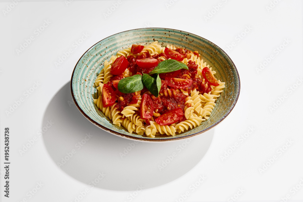 Fototapeta premium Fusilli pasta with tomato sauce, cherry tomatoes and basil served on ceramic plate on white background side view. Concept of italian cuisine, restaurant menu, food styling and healthy eating.
