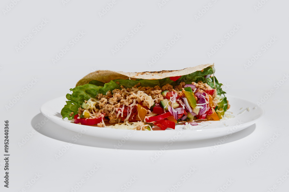 Fototapeta premium Side view tortilla wrap filled with vegetables, minced meat and cheese on white plate on clean background. Concept of fast dining, takeaway culture, delivery service and food choice in busy lifestyle.
