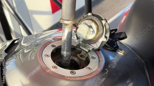 A man refuels his motorcycle, pouring gasoline through the tank opening in close-up. The scene captures the precise moment of filling up the gas tank.