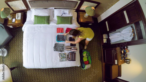 TOP DOWN: Female traveler opens her travel bag and unpacks her clothes onto bed