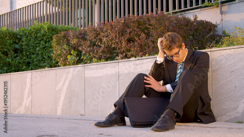 Valokuva Depressed young Caucasian yuppie sitting on the sidewalk after going bankrupt