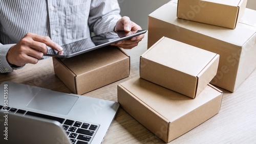 Close-up of a person using a tablet for business logistics, surrounded by packaging boxes and a laptop. Ideal for concepts of small business and delivery.