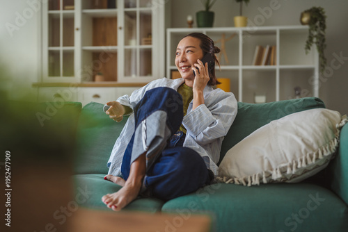 Fotografie Asian woman talking on smart phone smiling happily at home