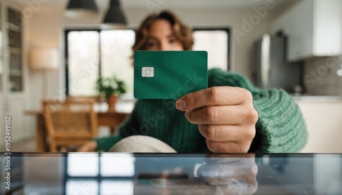 Hand holding a credit card above a utilities subscription autopay webpage with the users face and room softly blurred in the background.