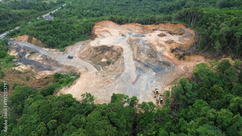 Canvas Print Aerial view of an open-pit mining site with excavators and trucks clearing land within a forested landscape