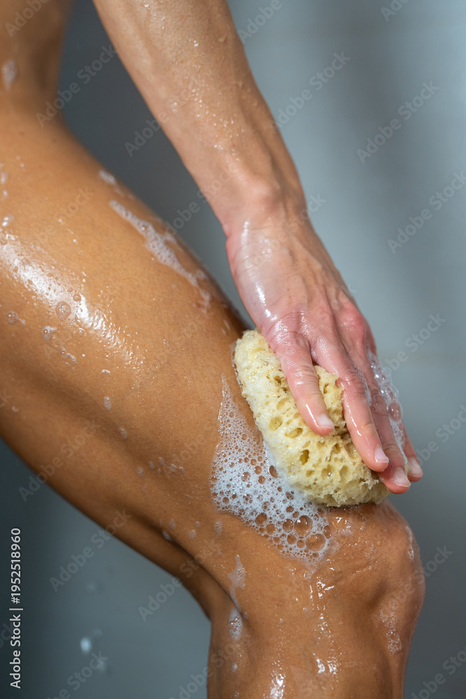 Fototapeta premium Woman washing leg with natural sponge in shower, body hygiene routine, skincare and wellness concept, daily cleansing, healthy lifestyle, self care, freshness