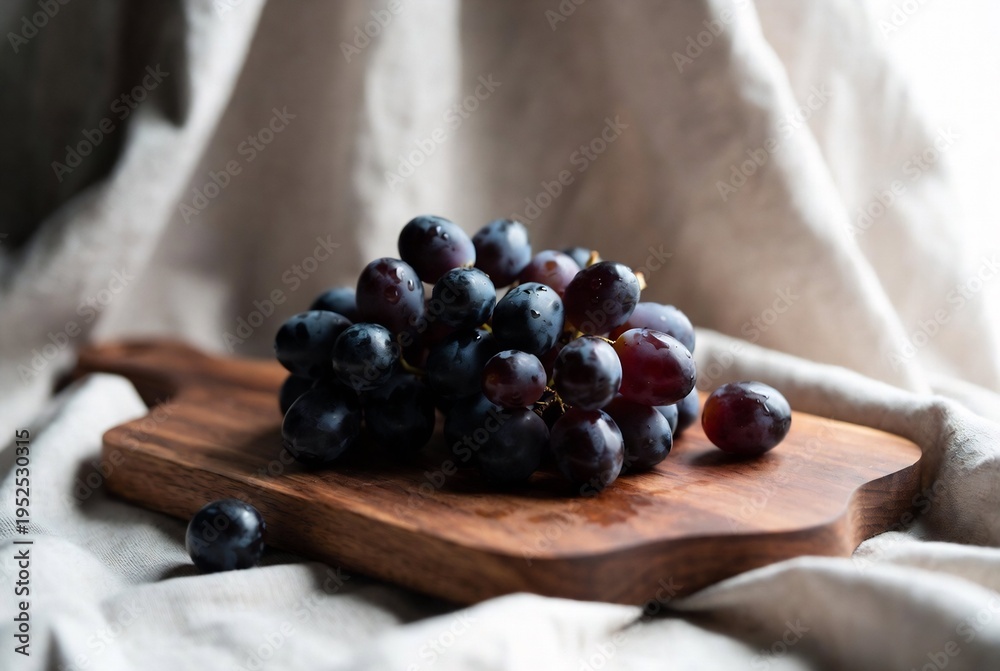 Fototapeta premium A cluster of dark grapes rests on a wooden board, draped with fabric.