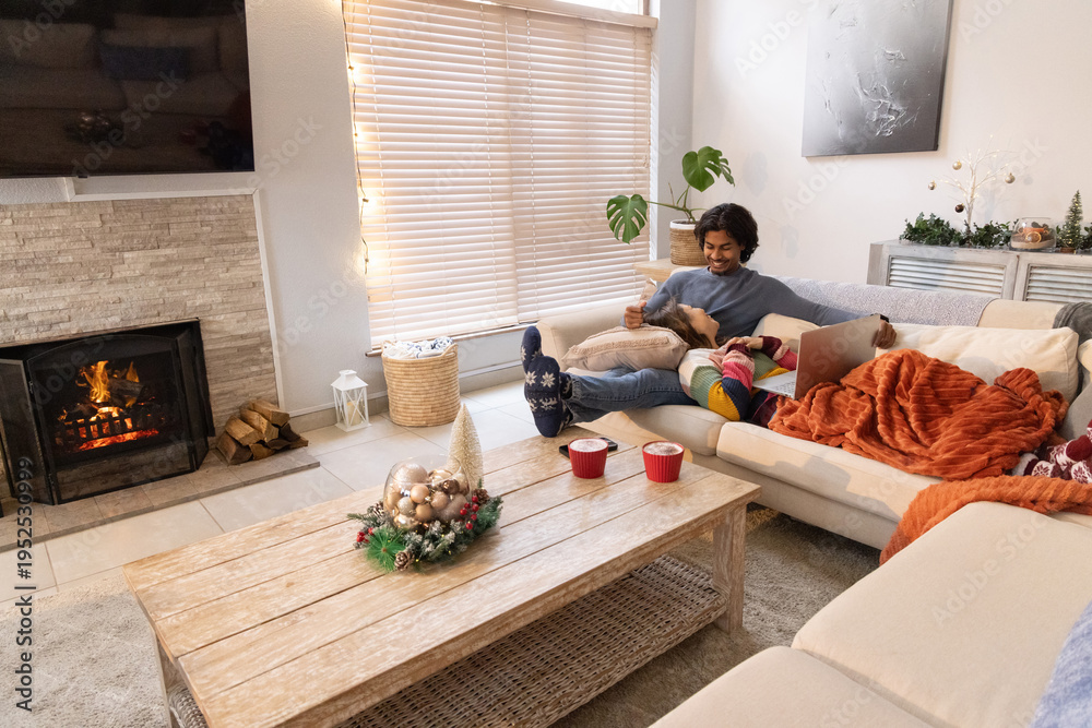 Obraz premium Couple sitting on right side of sectional sofa using laptop under orange blanket by fireplace