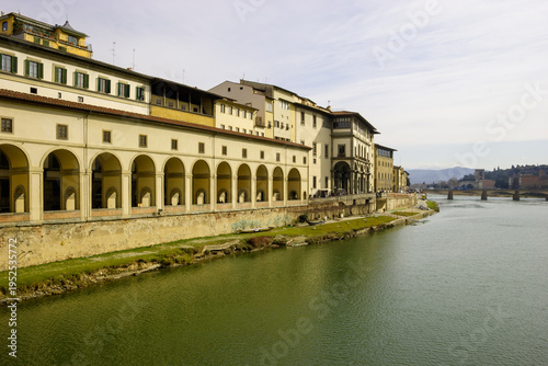 Tableau sur toile The Arno River flows past the Uffizi Gallery in Florence, Italy, with its distinctive arcades and historic architecture under a cloudy sky