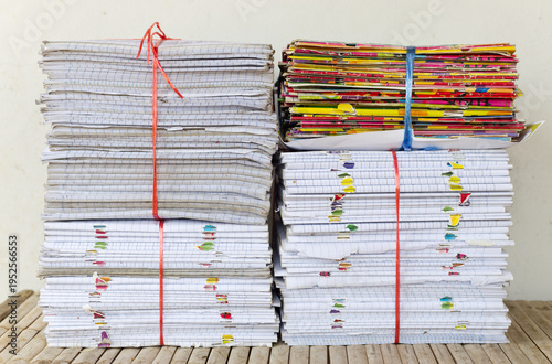 A front view of multiple stacks of old school notebooks and colorful books, securely tied with red and blue plastic ropes, ready for recycling or storage.