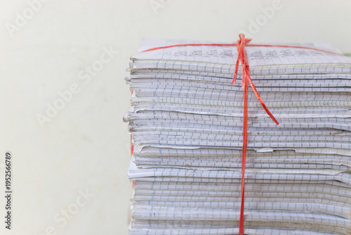 A front view of multiple stacks of old school notebooks and colorful books, securely tied with red and blue plastic ropes, ready for recycling or storage.