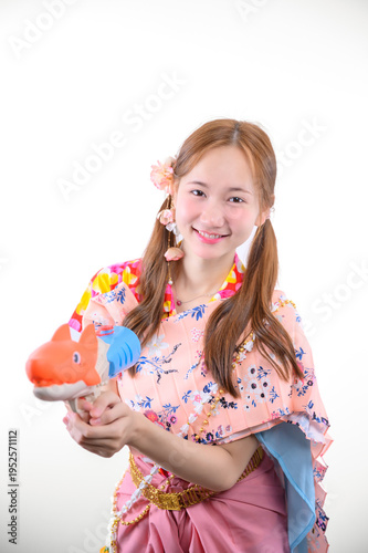 Cheerful Asian woman in a floral modified Thai traditional costume, combining a patterned blouse and a modern skirt, smiling and holding a water gun for Songkran Festival on white background.