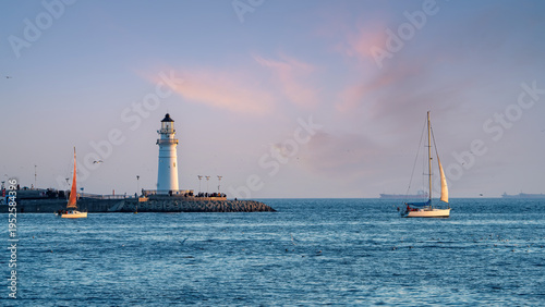 Lighthouse on Pier with Sailing Boats at Sunset