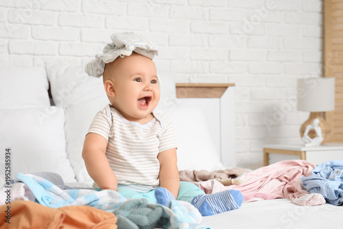 Cute little baby with scattered clothes in bedroom