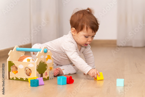 9-month-old baby girl focusing on picking up a toy from the floor at home.