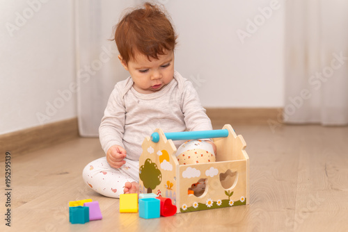 9-month-old infant girl sitting on the floor and playing with toys. 