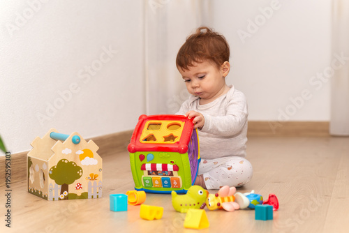 Sitting 9-month-old baby girl engaged in playtime with educational toys.