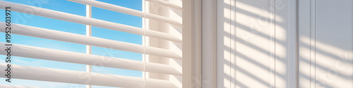 Automated window blinds partially open with sunlight casting striped shadows on white wall, creating calm and modern interior atmosphere