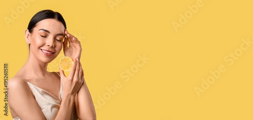 Quadro em tela Beautiful young woman holding lemon on yellow background with space for text