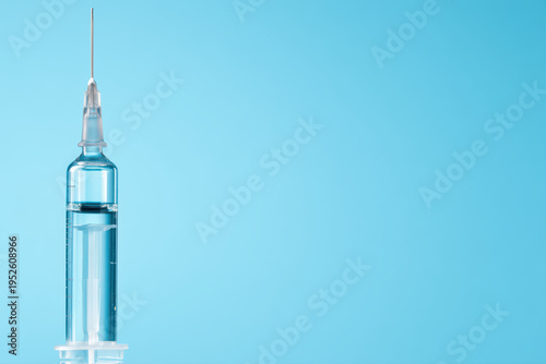 Syringe with clear liquid on blue background, medical injection tool for healthcare and vaccination, close up macro shot with minimal style and transparent details