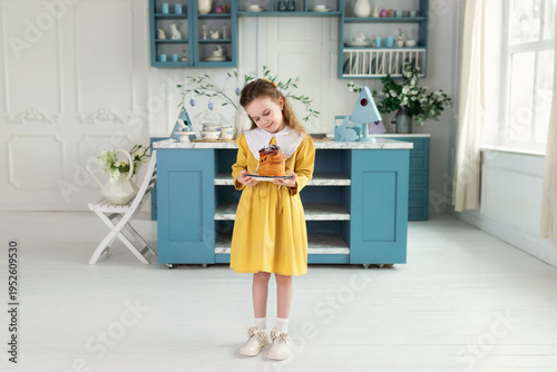 Wallpaper Mural Young cute girl with easter cake in hands. Smile child holding easter pastries, celebrating easter and spring. Happy little girl holding a baking with baked cake in her hands on festive house kitchen Torontodigital.ca