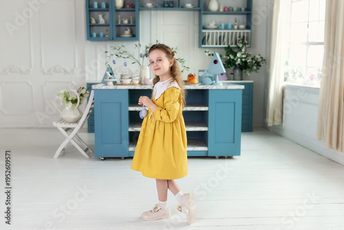 Wallpaper Mural Happy Little girl in yellow dress with collar holding Easter colorful eggs in hand in festive kitchen. Cute fun child Girl hunts easter eggs at home. Holiday, spring and family celebration concept. Torontodigital.ca