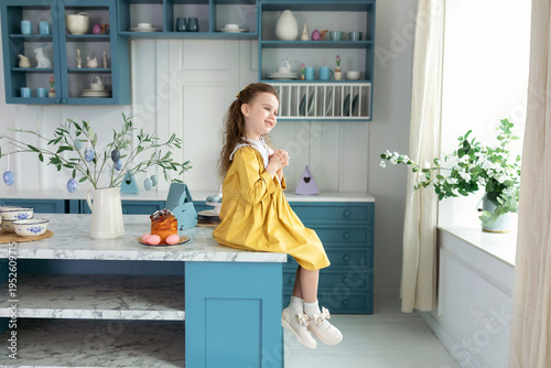 Wallpaper Mural Happy child girl praying, hands folded in prayer concept for faith, spirituality and religion. Smiling little blond girl in a yellow dress on kitchen with easter cake, flowers, easter eggs, bunny. Torontodigital.ca