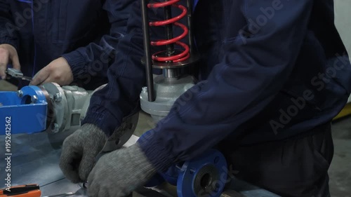 Worker's gloved hands installing red spring mechanism into blue industrial valve, technical manufacturing process