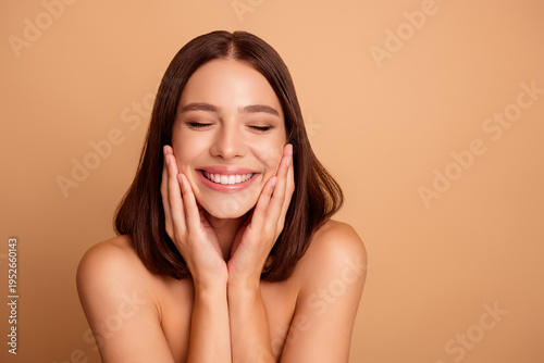 Canvas Print Smiling brunette woman cups her face with hands against a warm beige backdrop id