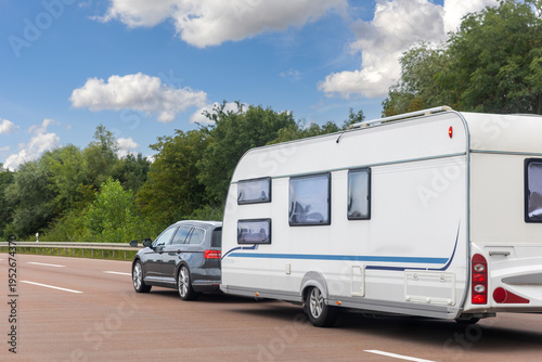 Scenic view big modern white family car tow rv camper vehicle drive Europe highway road freeway drive cloud in summer day. Rving motorhome lifestyle travel and adventure tourism trip journey concept