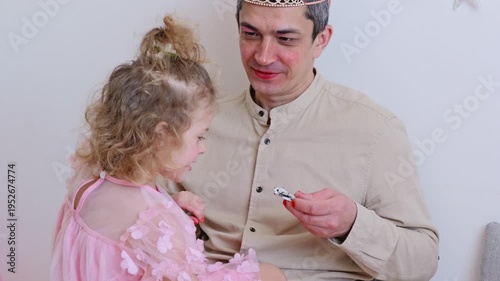 A father and his daughter share a playful time in a warm room. They engage in activities with toys and dress-up items, creating happy moments together