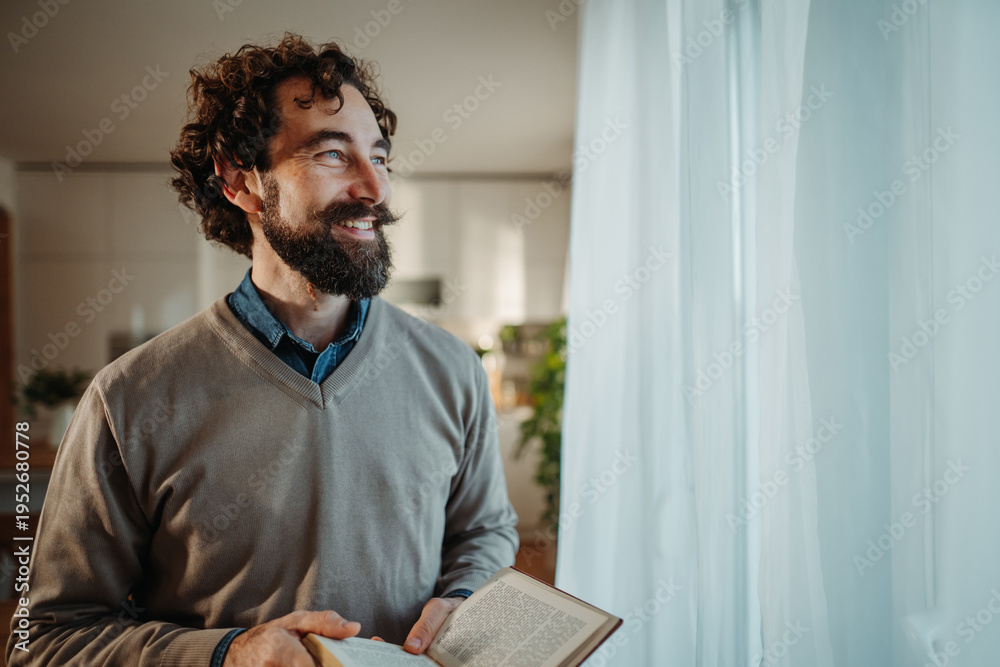 Fototapeta premium Happy man reading book looking out window
