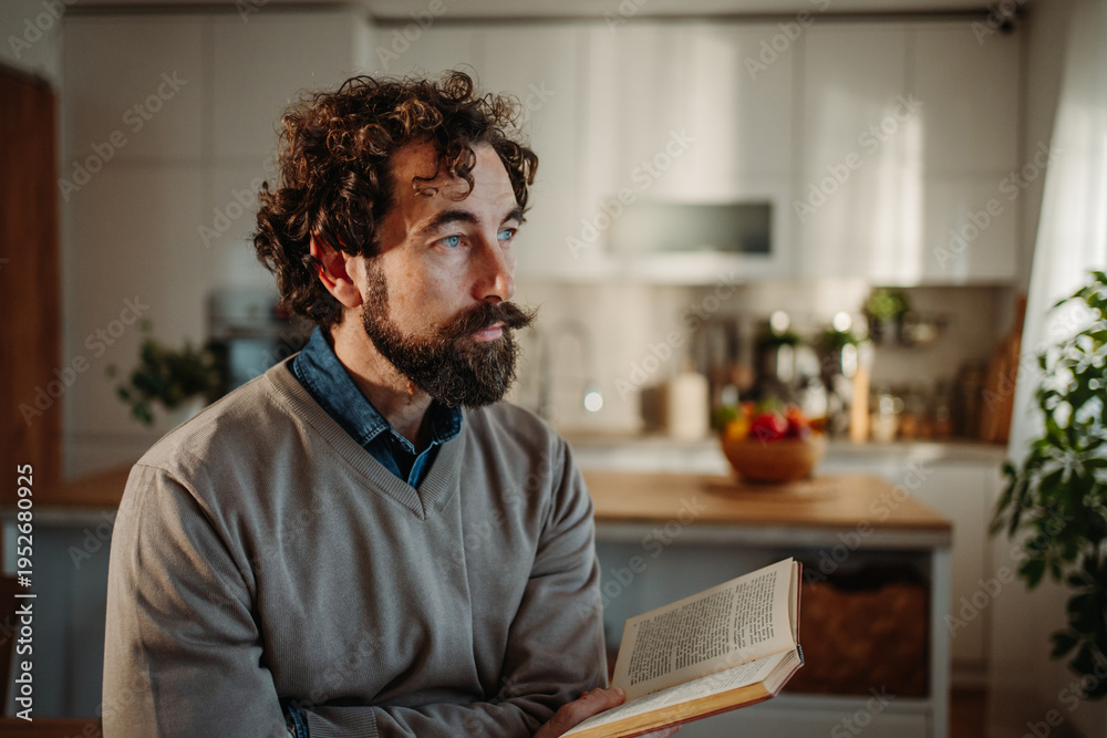 Fototapeta premium Man with curly hair reading, contemplating in kitchen
