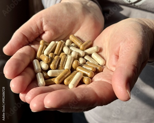 Close-up of a woman holding mixed medicine capsules, beige and brown pills in her open palms, soft light in the room, contemplative mood