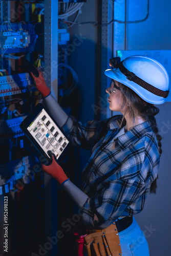Female electrician inspecting electrical panel with tablet in server room. Power engineer.