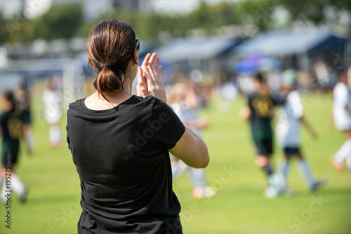 Asian parents watching and supporting their children playing football on a sunny afternoon at a local community tournament.