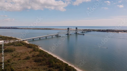 Aerial drone view of Marine Parkway Bridge spanning calm coastal water with surrounding shoreline and breakwater under a soft cloudy sky.