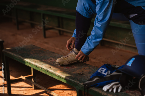 Quadro su tela Male baseball or softball player tying the laces of his cleats on a bench before a game