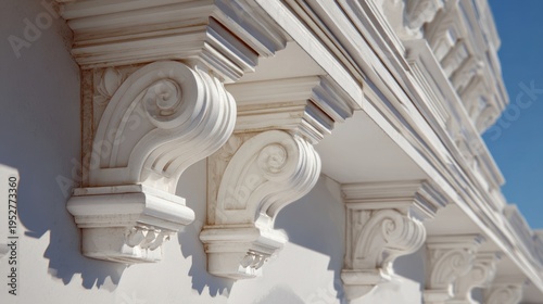 White classical architectural corbels with ornate scroll patterns support a balcony under a bright blue sky on a sunny day.
