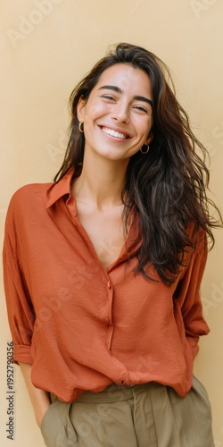 Young hispanic female adult smiling by yellow wall wearing rust blouse and olive pants casual portrait lifestyle