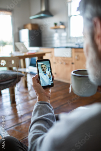 Senior man on telehealth video call with doctor in home kitchen