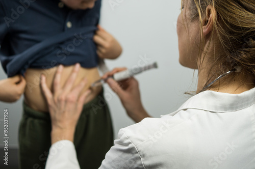 Macro shot of a doctor's hands carefully pinching the skin and administering a dose of medication into the abdomen of a child.
