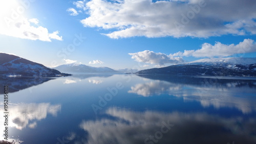 Quadro su tela Aerial drone view of calm Norwegian fjord reflecting snowy mountains and dramatic clouds under blue sky