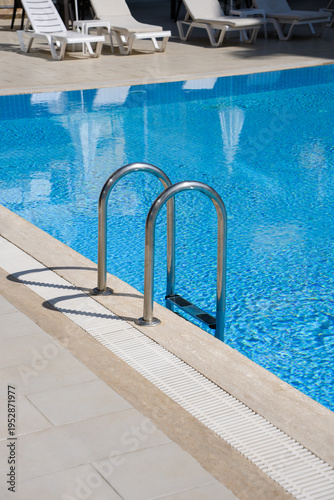 Sunlit staircase leading to swimming pool with sparkling blue water and sun loungers in background. Pool area. Relaxation and leisure concept, hotel vacation.