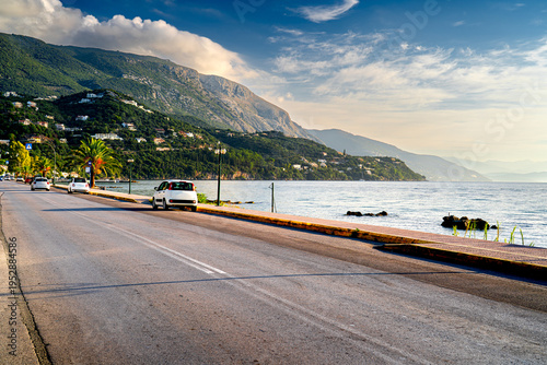 Coast Greek island Corfu with cars and mountains in morning light.