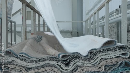 Industrial carpet manufacturing process showing stacks of finished rugs in a factory warehouse setting.