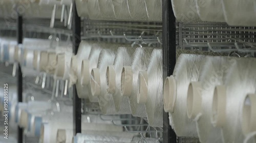 High angle perspective of rows of colorful yarn bobbins on an automated carpet manufacturing factory floor.