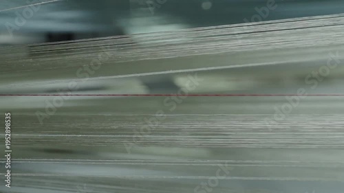 Close up of white synthetic fibers moving rapidly through an industrial weaving machine with a single red thread.