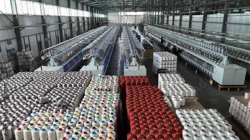 Wide view of a large industrial textile factory with rows of spinning machines and stacks of colorful yarn spools.