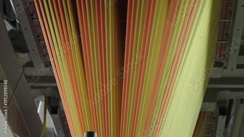 Close up of vibrant orange and yellow synthetic fibers moving through an industrial loom in a carpet factory.